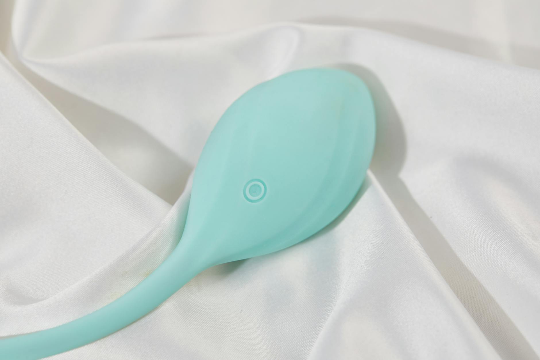 Ein stylischer türkiser Vibrator auf glatter weißer Seide, perfekt für Wellness und Selbstpflege.