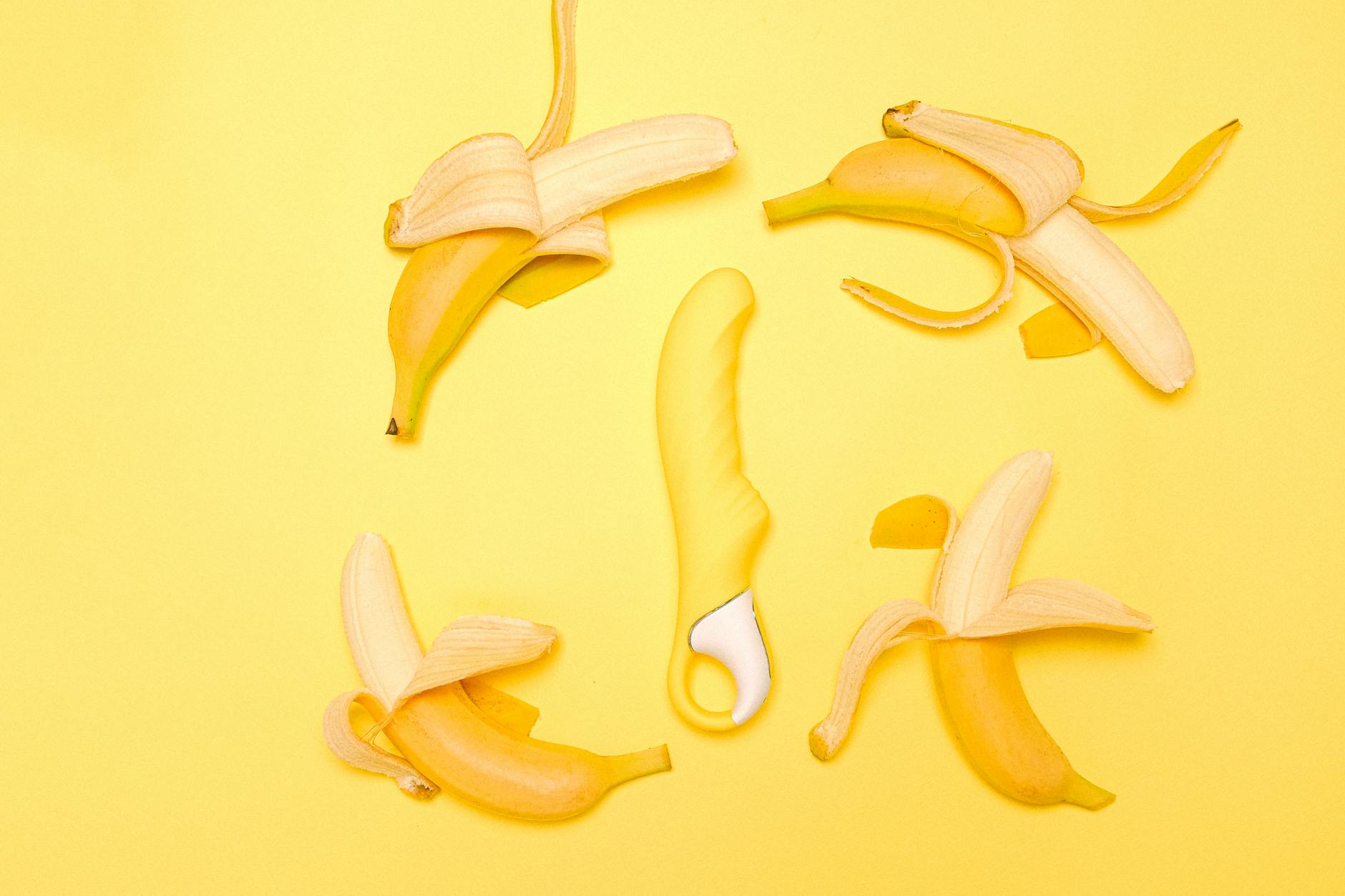 Ein gelber Silikonvibrator umgeben von geschälten Bananen auf gelbem Hintergrund
