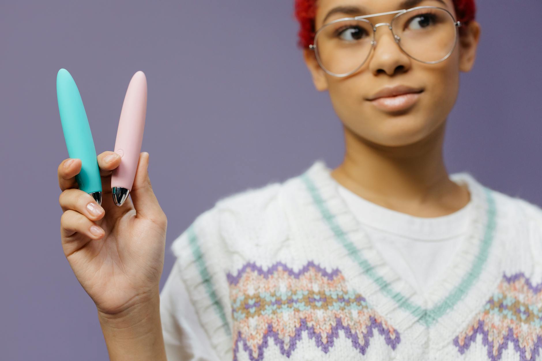 Frauenhände halten zwei farbenfrohe Vibratoren vor einem violetten Hintergrund