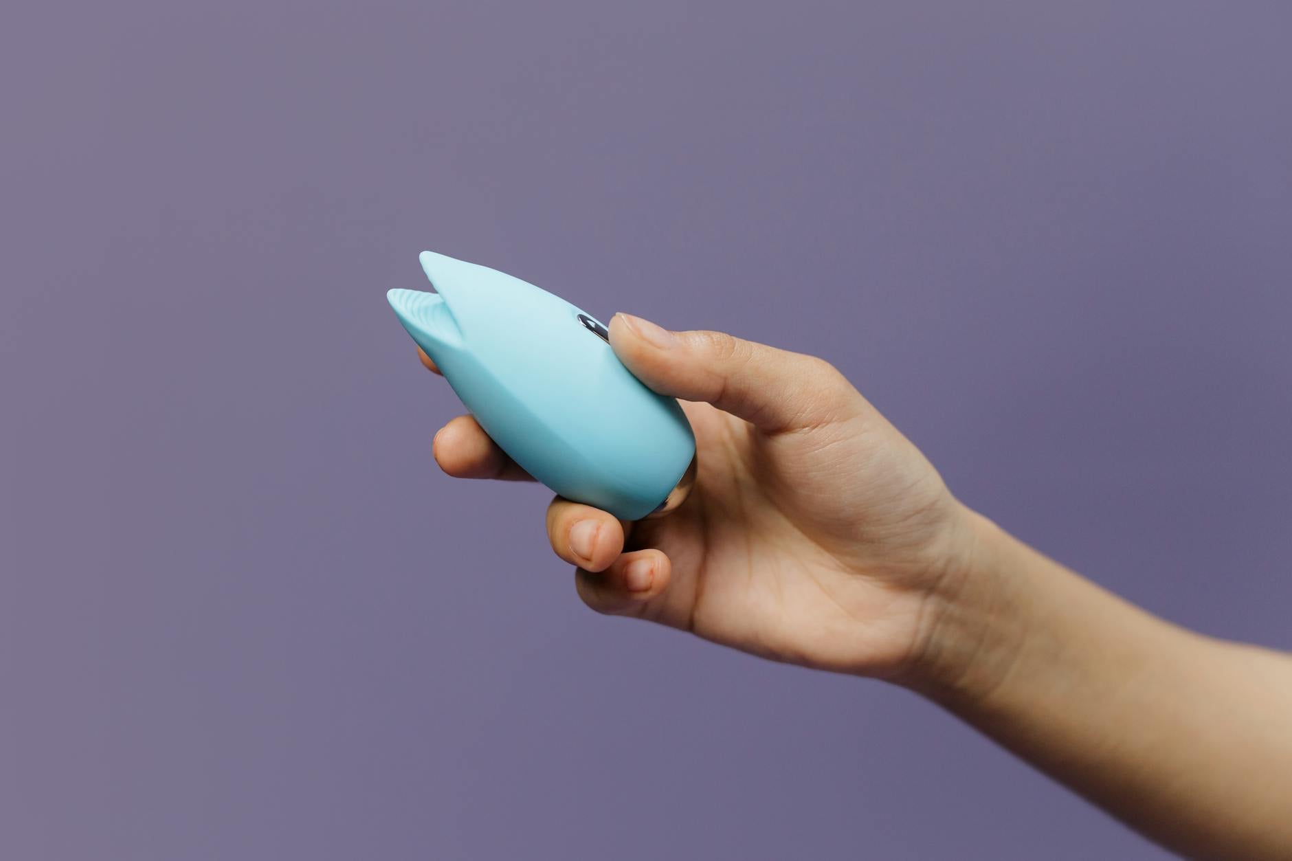Ein blauer Silikonvibrator in der Hand gegen einen lila Hintergrund, der Selbstliebe und Sexualität fördert