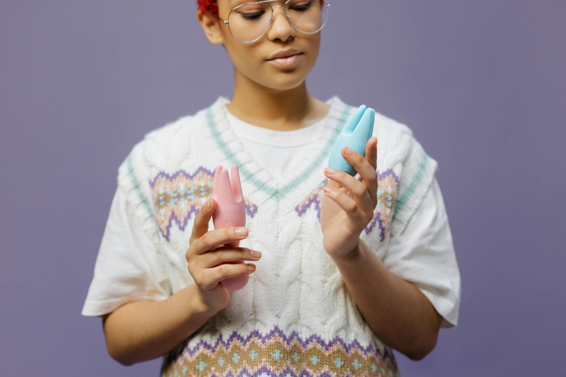 Frau mit Brille hält einen blauen und rosa Silikon-Vibrator in nachdenklicher Pose