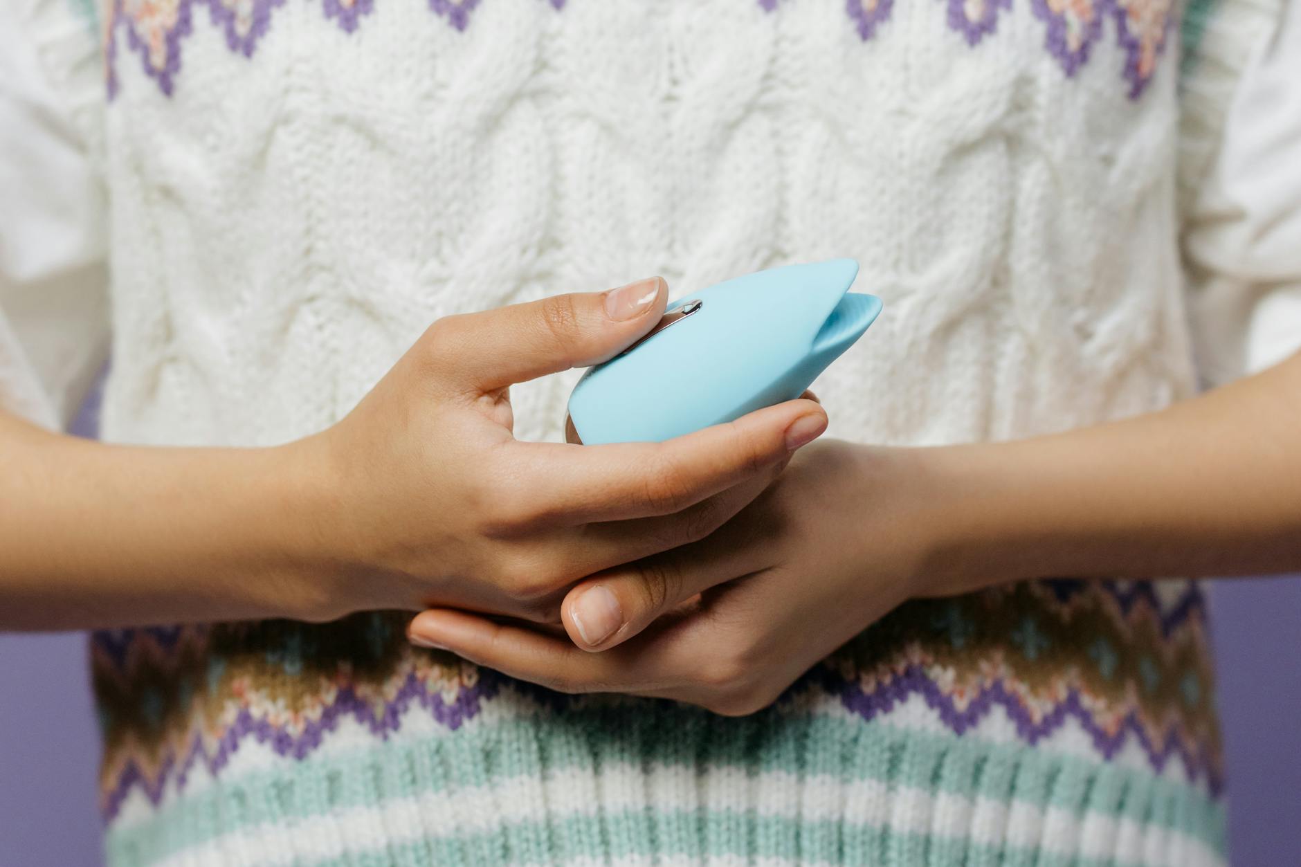 Nahaufnahme von Händen, die einen blauen Personal Massager gegen einen gestrickten Pullover halten